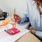 Femme écrivant sur un papier avec un crayon, calculatrice rouge, documents, bureau, intérieur