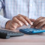 Personnes mains au clavier et à la calculatrice sur un bureau avec tasse et plante