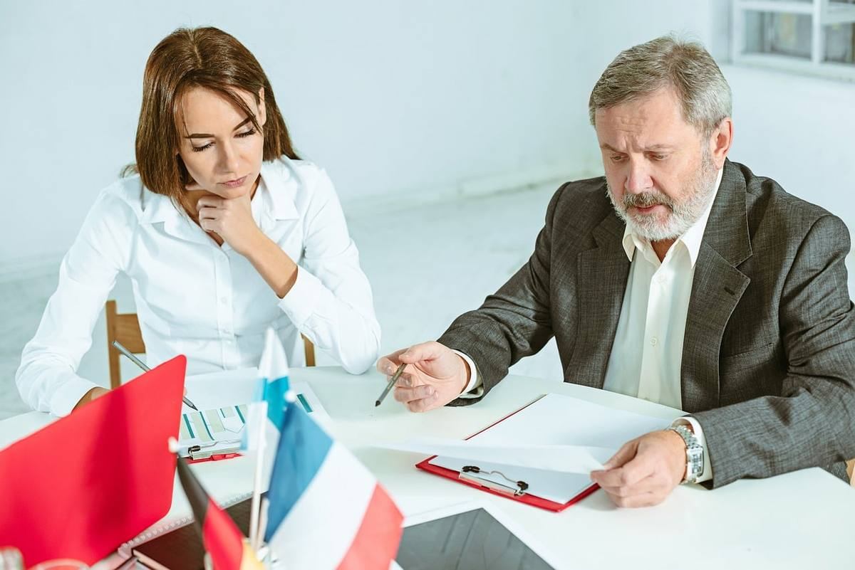 Deux professionnels discutent autour d'un bureau avec documents, représentant une négociation commerciale
