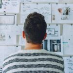 Homme observant un mur couvert de documents, schémas et wireframes de projet