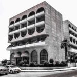 Immeuble moderne à arcs, voitures sur la rue, palmier, ciel nuageux