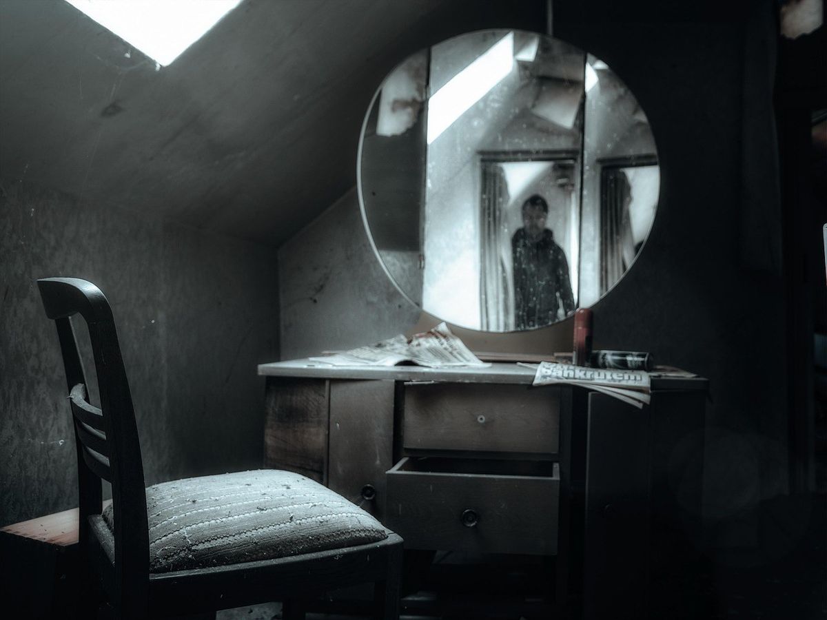 Miroir reflétant une personne dans une pièce sombre avec bureau et chaise