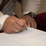 Mains écrivant sur un document avec un stylo, montre et anneau visibles