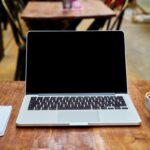 Ordinateur portable blanc ouvert sur un bureau en bois avec une tasse de café et un bloc-notes