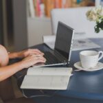 Une femme travaille à distance, écrivant sur ordinateur, avec notes et café